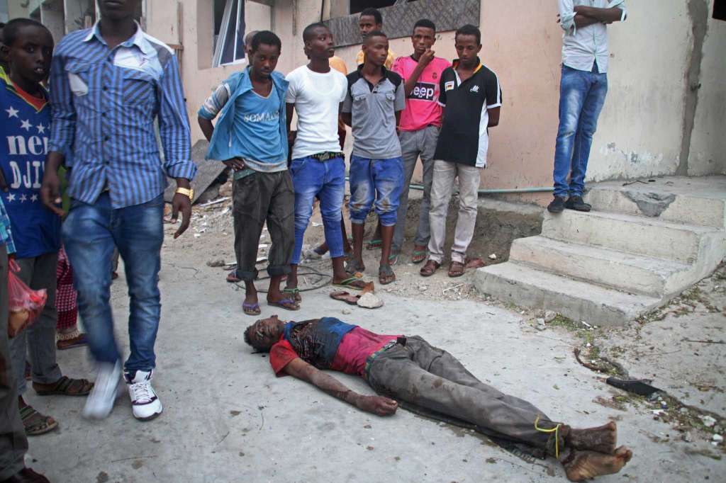 Somalis gather around a dead civilian victim during an attack on a hotel in Mogadishu, Somalia, Saturday, June 25, 2016. A Somali police officer says a suicide car bomber detonated an explosives-laden vehicle at the hotel gate followed by gunmen who fought their way into the hotel and took an unknown number of hotel guests hostage.