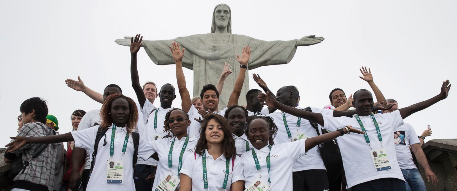 Athletes of the Refugee Olympic Team take pictures with a staff member in front of the statue of Christ the Redeemer
